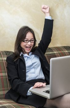 Professional woman in business suit on sofa cheering with fists in air with laptop 