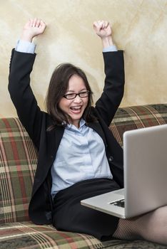 Professional woman in business suit on sofa cheering with fists in air with laptop 