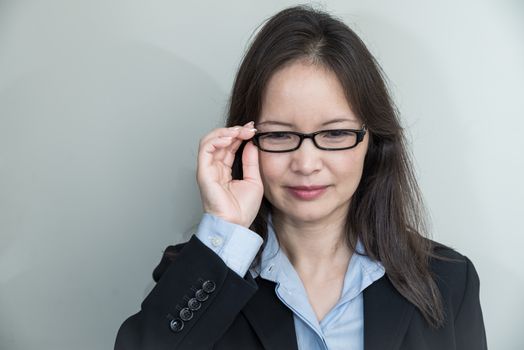 Portrait of woman with glasses in business suit smiling on grey background 