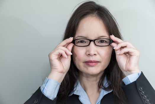 Portrait of woman with glasses in business suit smiling on grey background 