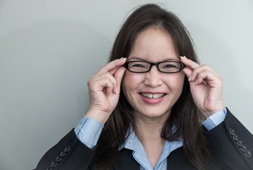 Portrait of woman with glasses in business suit smiling on grey background 