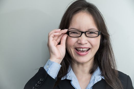 Portrait of woman with glasses in business suit smiling on grey background 