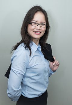 Professional woman in business casual with jacket on her shoulder on grey background