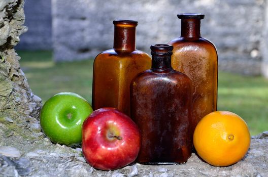 Old brown bottles sit along side fresh apples and an orange in a ledge of tabby ruins