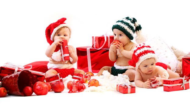Three babies in xmas costumes playing with gifts over white background