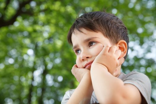 Sad little boy looking at something against blurred natural background