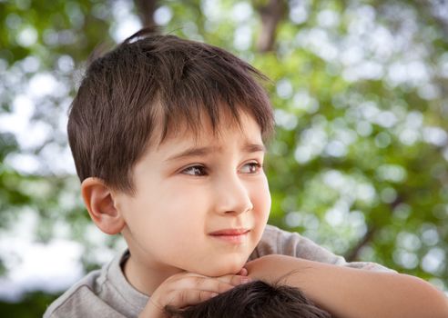 Sad little boy looking at something against blurred natural background