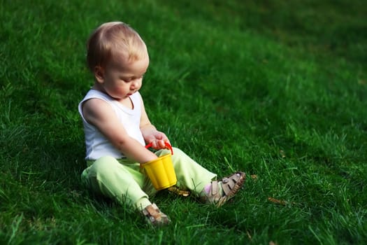 Little boy with pail sits on a green grass