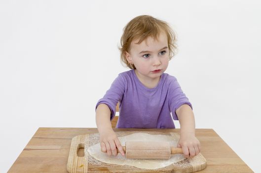 child rolling out dough on small desk. studio shot on grey background