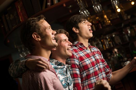 Three men stand in a row embracing smile and look in front of you, sports fans