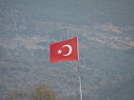 Raised Turkish flag flies in the wind against the background of mountains