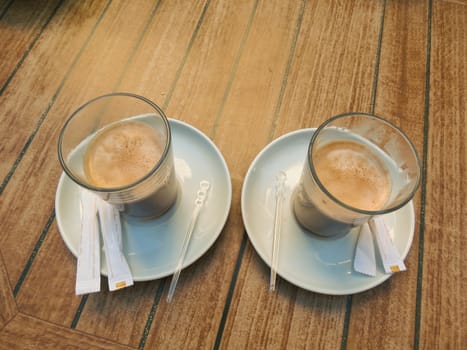 On the table are two white saucers glass cup of cappuccino