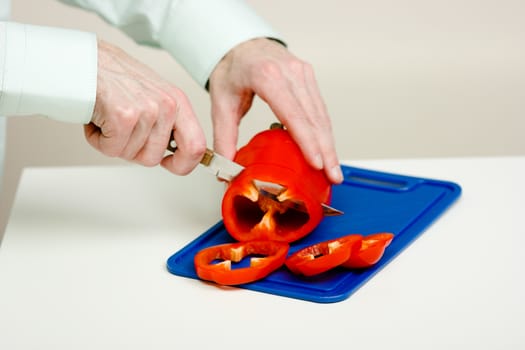 Man's hand cut red pepper on a cutting board