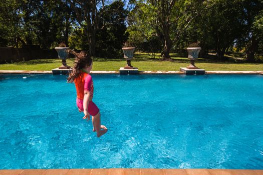 Young girl having fun jumping into summer blue swimming pool.