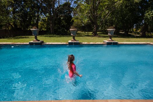 Young girl having fun jumping into summer blue swimming pool.