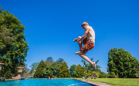 Teen boy jumping to make large water splash in home swimming pool.