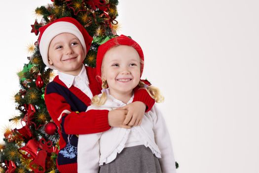 Little sister and brother hugging under Christmas tree over light grey back