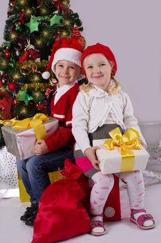 Smiling little girl and boy sitting with gift under Christmas tree