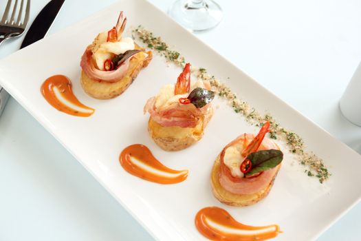 Delicious and delicate shrimps wrapped in bacon on potato slices with a spinach leaf.