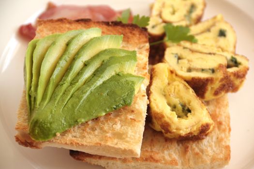 Sliced avocado on toasty Turkish bread with rolled omelette ready to serve.