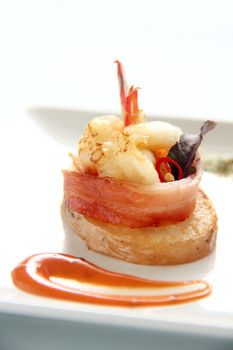 Delicious and delicate shrimps wrapped in bacon on potato slices with a spinach leaf.
