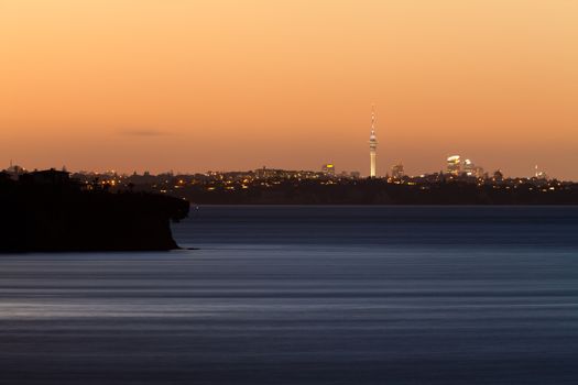 Distant skyline of Auckland City, New Zealand, with Sky Tower illuminated in twilight dusk after sunset