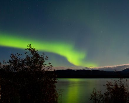 Band of green northern lights, Aurora borealis, on night sky mirrored on Lake Laberge, Yukon Territory, Canada