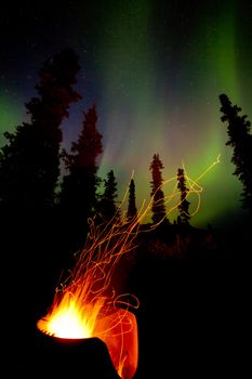 Open campfire burning hot in cast iron fire pit with spark trails flying off into boreal forest taiga under northern lights, Aurora borealis