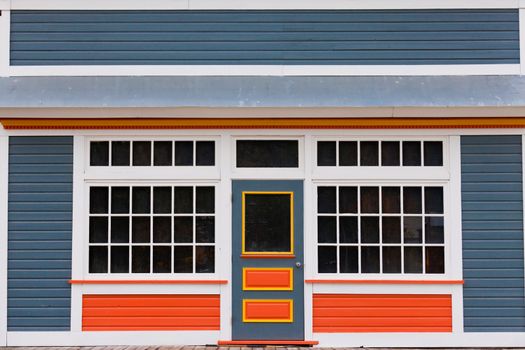 Symmetrical view of the front door and entrance to a quaint colorful wooden house with large cottage pane windows on either side