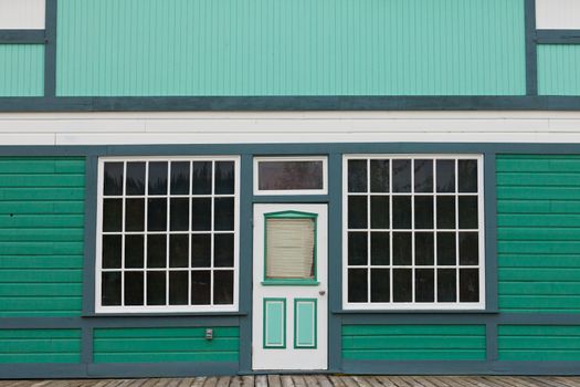 Symmetrical view of the front door and entrance to a quaint green wooden house with large cottage pane windows on either side