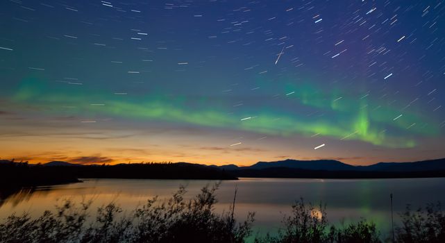 Northern lights Aurora borealis and shooting star meteor at midnight in summer over northern horizon of Lake Laberge Yukon Territory Canada at early dawn
