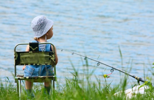 Little boy with fishng rod sitting near the lake