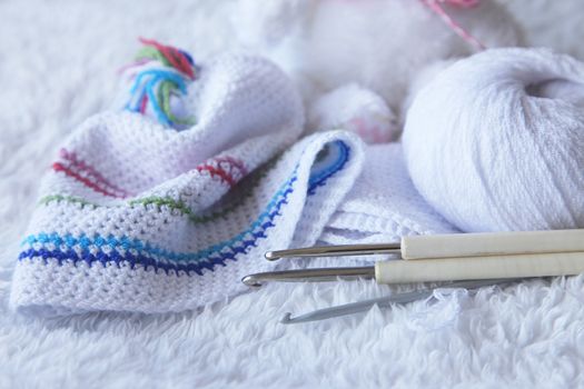 Baby hat from viscose and knitting hooks. Needlework accessories isolated on white background.