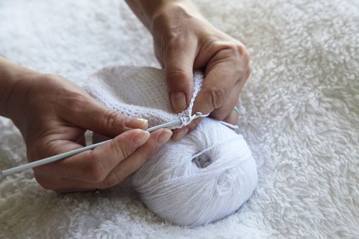 Hands of a adult woman knitting with white viscose