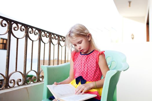 small girl reading book on the balcony