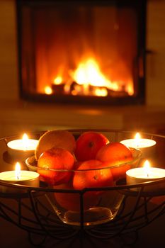 Fruits and candles in iron basket nearby fireplace