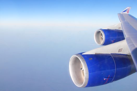 Turbine of passenger airplane flying in blue sky over clouds