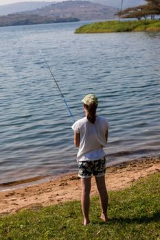 Girl fishing along shoreline of dam waters.