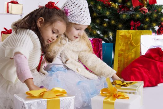 Two lovely little girls with presents under Christmas tree