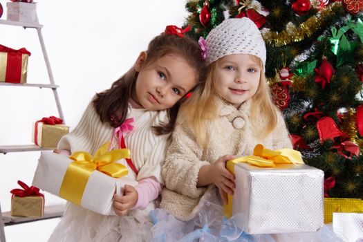 Two cute little sisters with presents under Christmas tree isolated over white