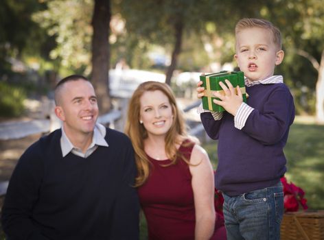 Handsome Young Boy Holding a Christmas Gift in the Park While His Mom and Dad Look On.