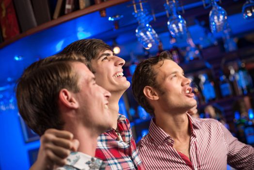 Three men stand in a row embracing smile and look in front of you, sports fans