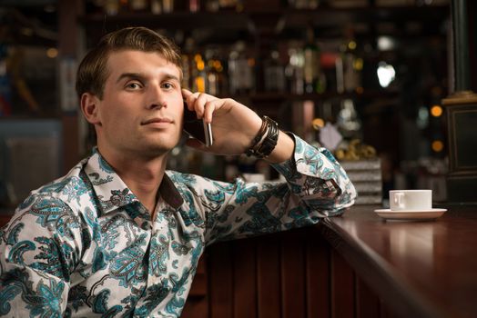 young man at the bar on the phone and drinking coffee