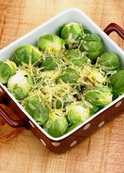 Brussels Sprouts Casserole in Brown Polka Dot Bowl with Grated Cheese and Spices closeup on Wooden background