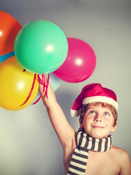 boy in Santa Claus hat holding balloons