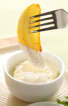 Crispy cooked potato wedge being dipped in sour cream.