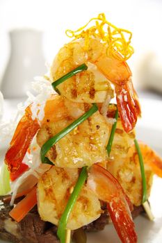 Stack of chargrilled shrimps tied up with chives on top of a grilled steak.