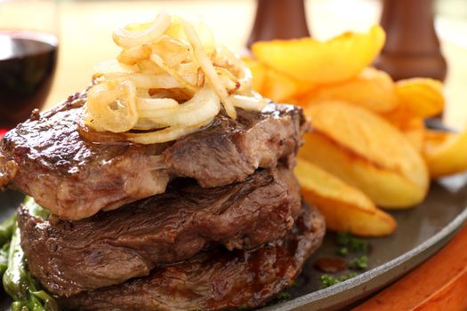 Fried onions on top of a stack of beef steaks.