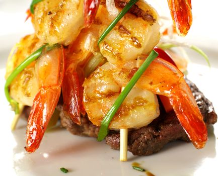 Stack of chargrilled shrimps tied up with chives on top of a grilled steak.