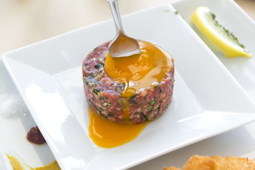 Fork piercing the yolk of the egg in a steak tartare.